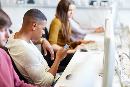 Student reading smartphone texts in higher education college computer room.